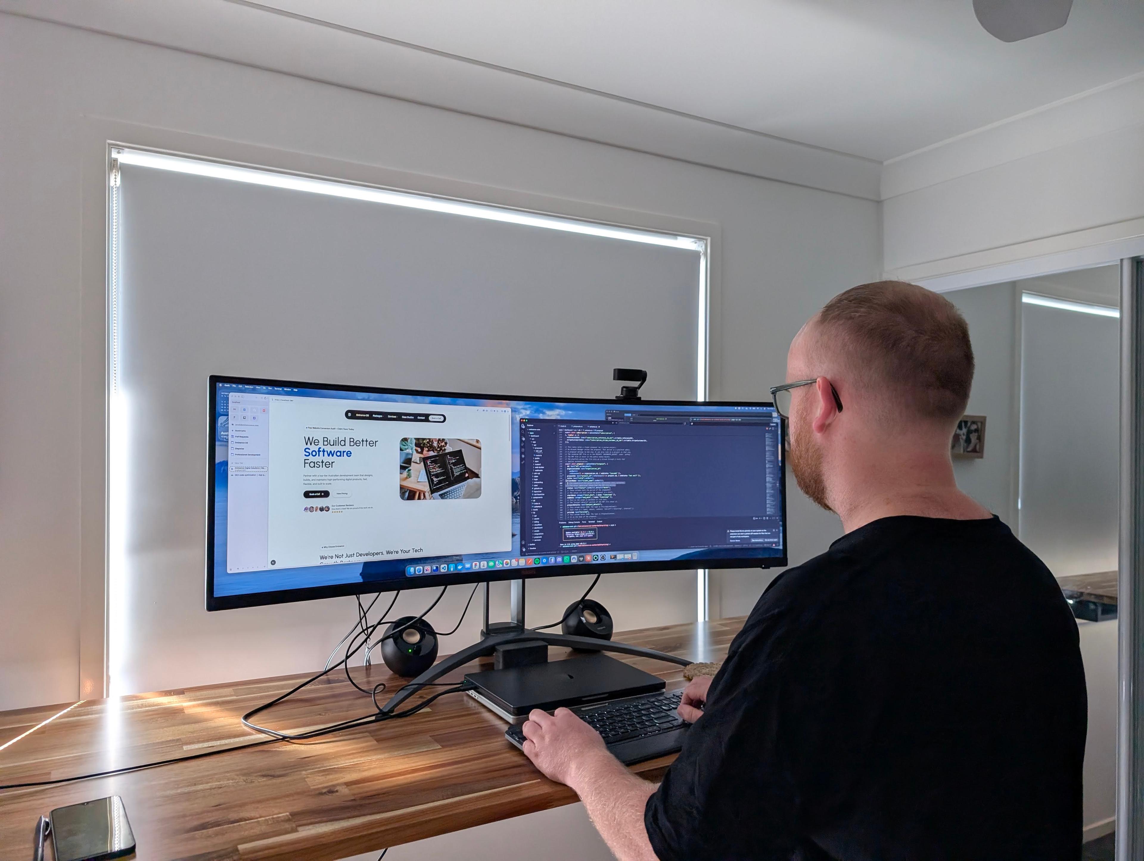 An Eminence Digital Solutions developer reviewing work on an ultrawide monitor at a timber desk